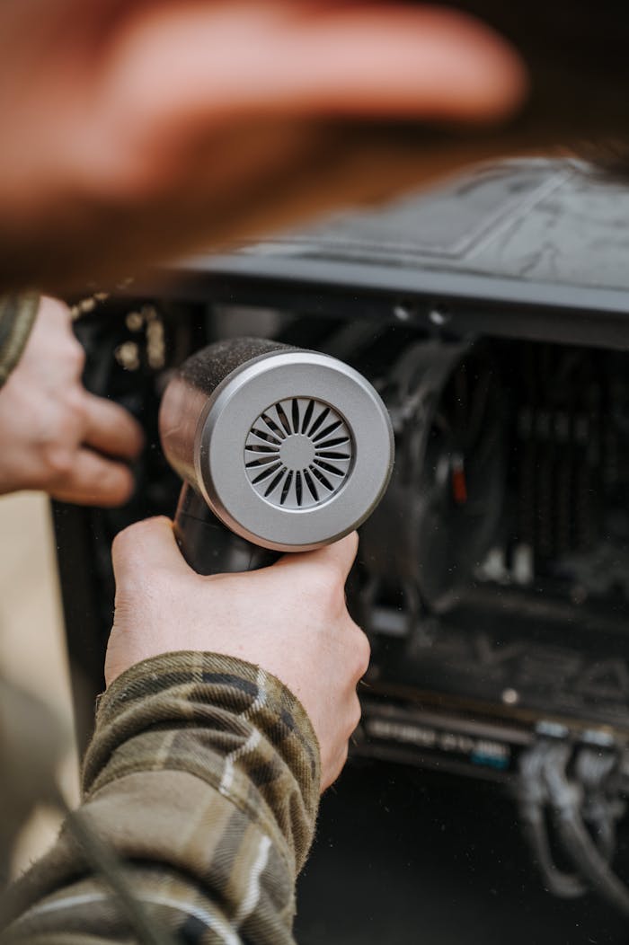 Close-up of an adult cleaning a computer's interior with an air duster for maintenance.
